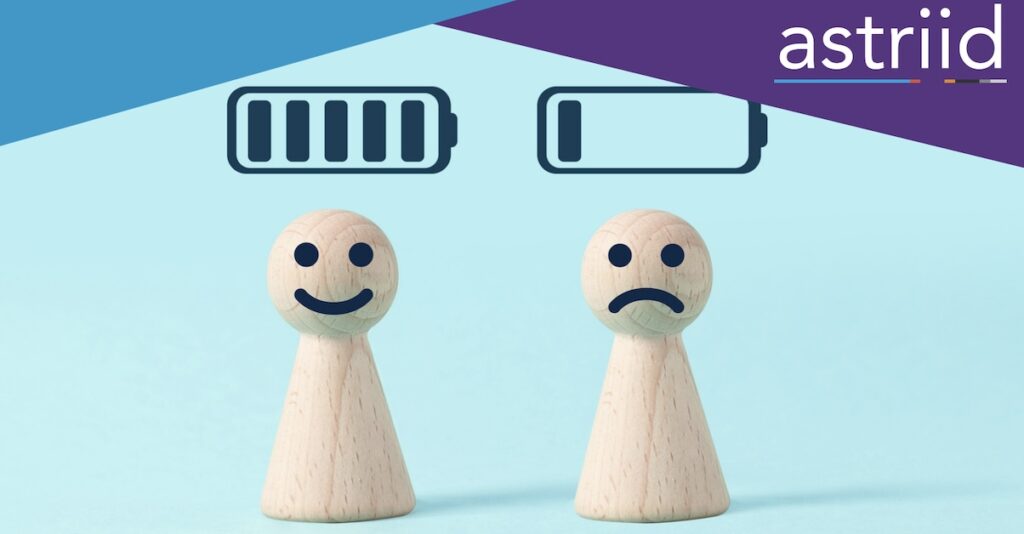 Two wooden figures of people stood next to each other. One is smiling with a full battery symbol over their head, the other is frowning with a low battery signal over their head, to represent energy limiting conditions.