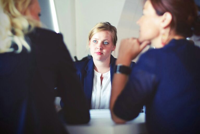 A woman sat across a desk from two managers, looking worried as they talk between them, to represent disability discrimination.