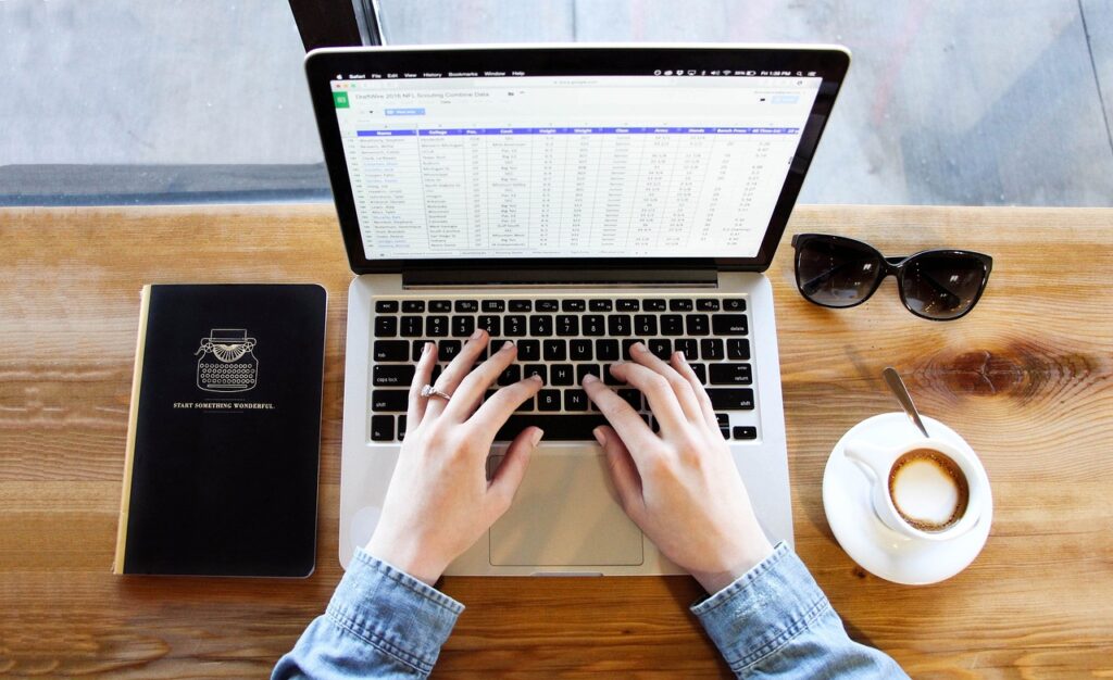 Hands typing on a laptop on a desk with a coffee and notebook next to it, to represent technology giant Salesforce.